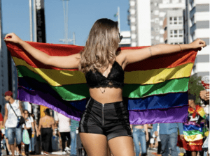 woman holding up gay pride flag at pride parade - clothes for pride featured image